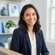 A diverse woman smiling in a bright, modern office space with blue-toned decor.
